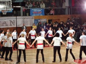 Хоро в кръг на напредналата група на клуб „Нашенци“ – Русе с бели туники и червени пояси на Коледното надиграване в Русе, 2011